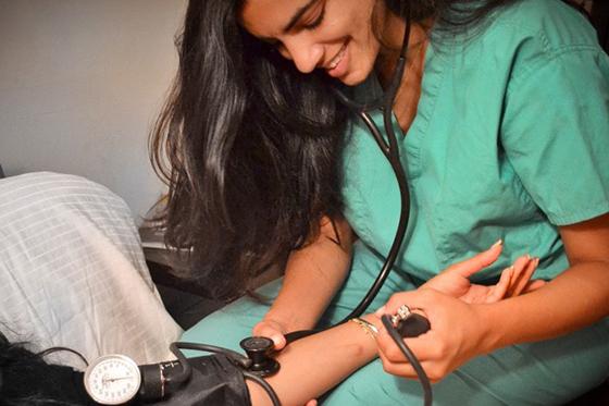 Photo of a nurse in green scrubs taking a patient's blood pressure with a stethoscope. 