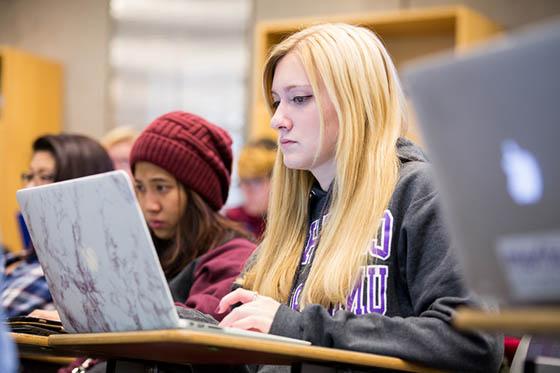 Photo of students paying attention in a lecture hall with computers in front of them